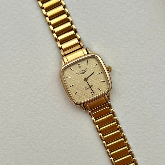 Longines soft-square gold-tone ladies watch with pale waffle-texture dial and integrated bracelet, displayed on a waffle background.