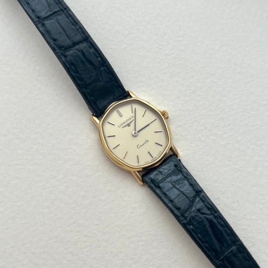 Longines soft tonneau gold-tone ladies watch with cream dial and black croc-embossed strap shown on the wrist.