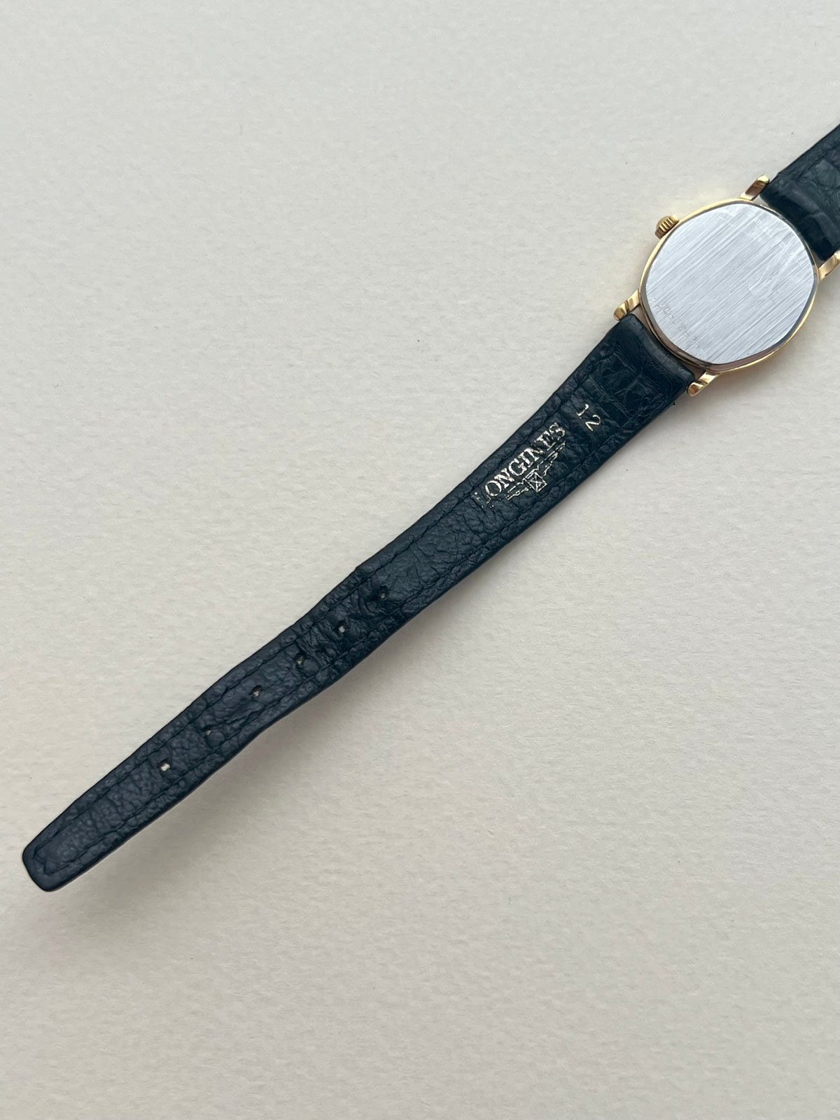 Side angle showing the curved gold-tone case of the Longines soft tonneau watch.