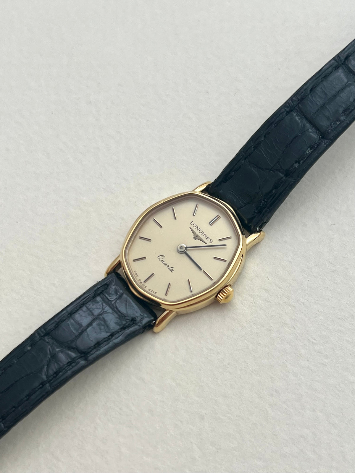 Longines gold-tone soft tonneau watch with original black leather strap worn on the wrist.