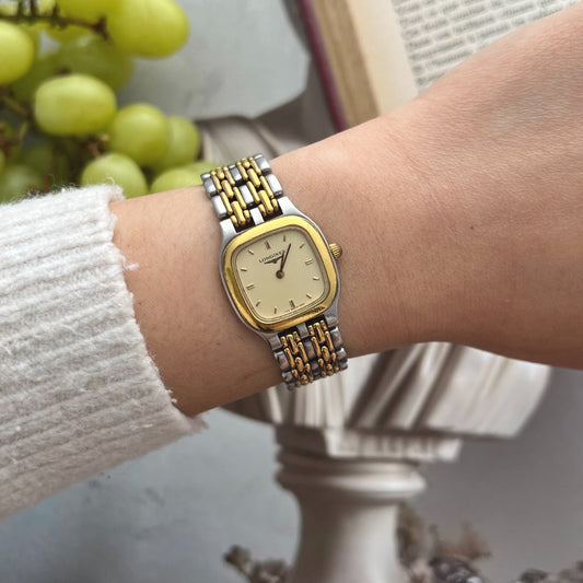 Longines women's cushion watch with a champagne dial, gold tone bezel and two tone bracelet worn on the wrist
