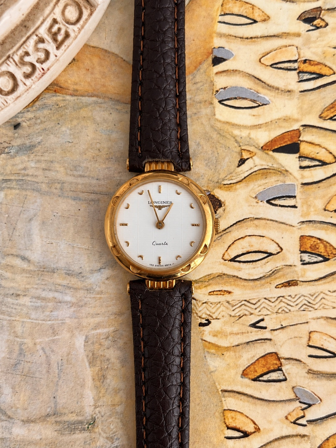 Front view of the Longines white patterned dial watch with gold tone crescent markers, decorated bezel and dark brown leather strap.
