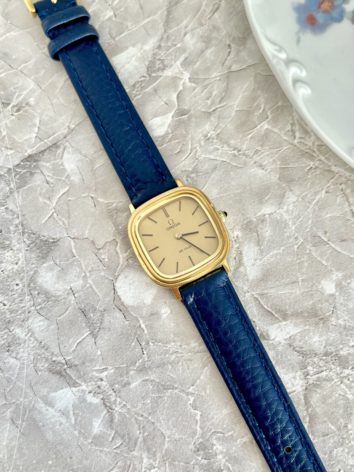 Omega De Ville square cushion watch with champagne dial, gold-tone case and navy blue textured strap