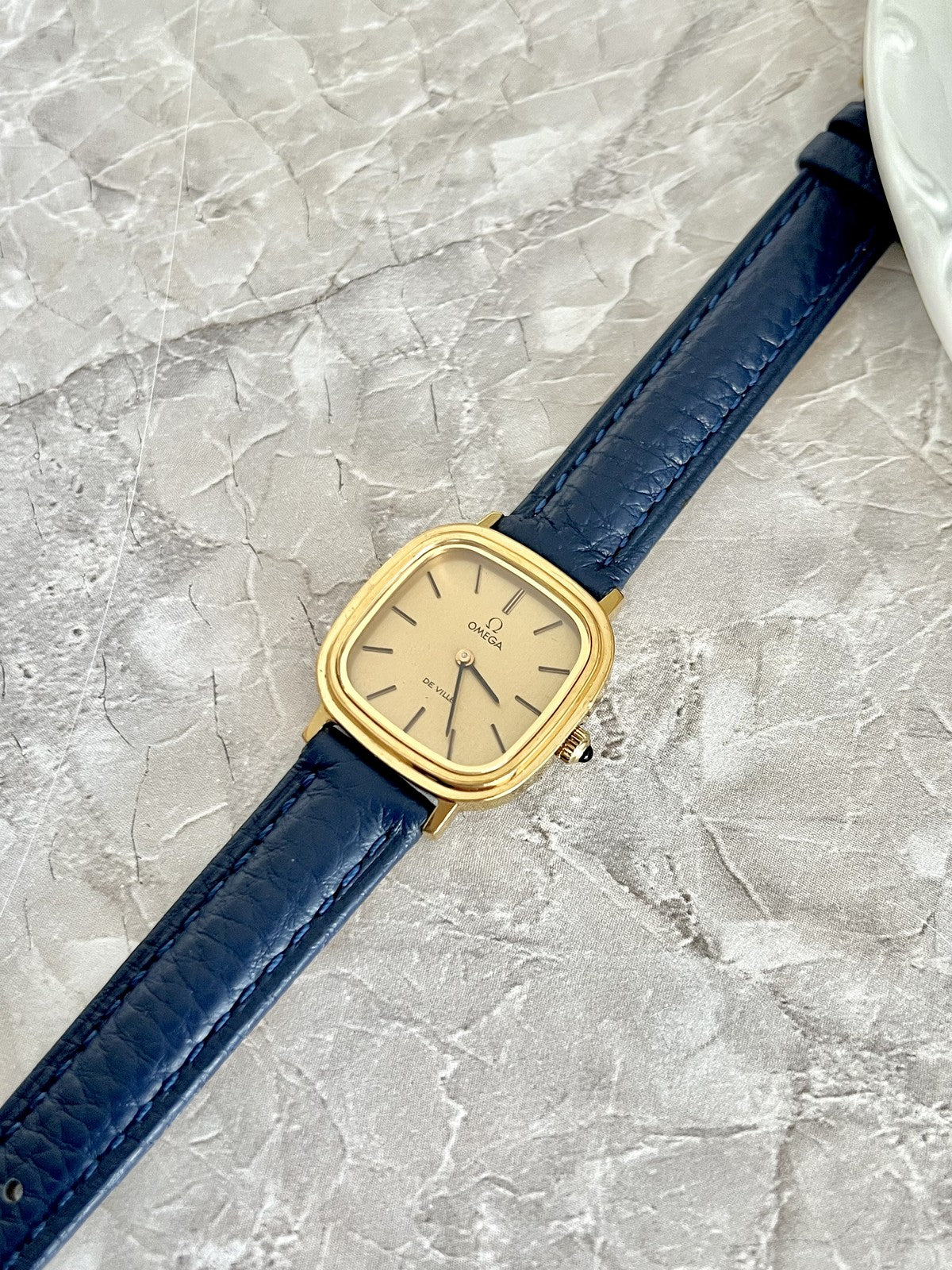 Three-quarter view of Omega De Ville gold-tone cushion watch and blue textured strap