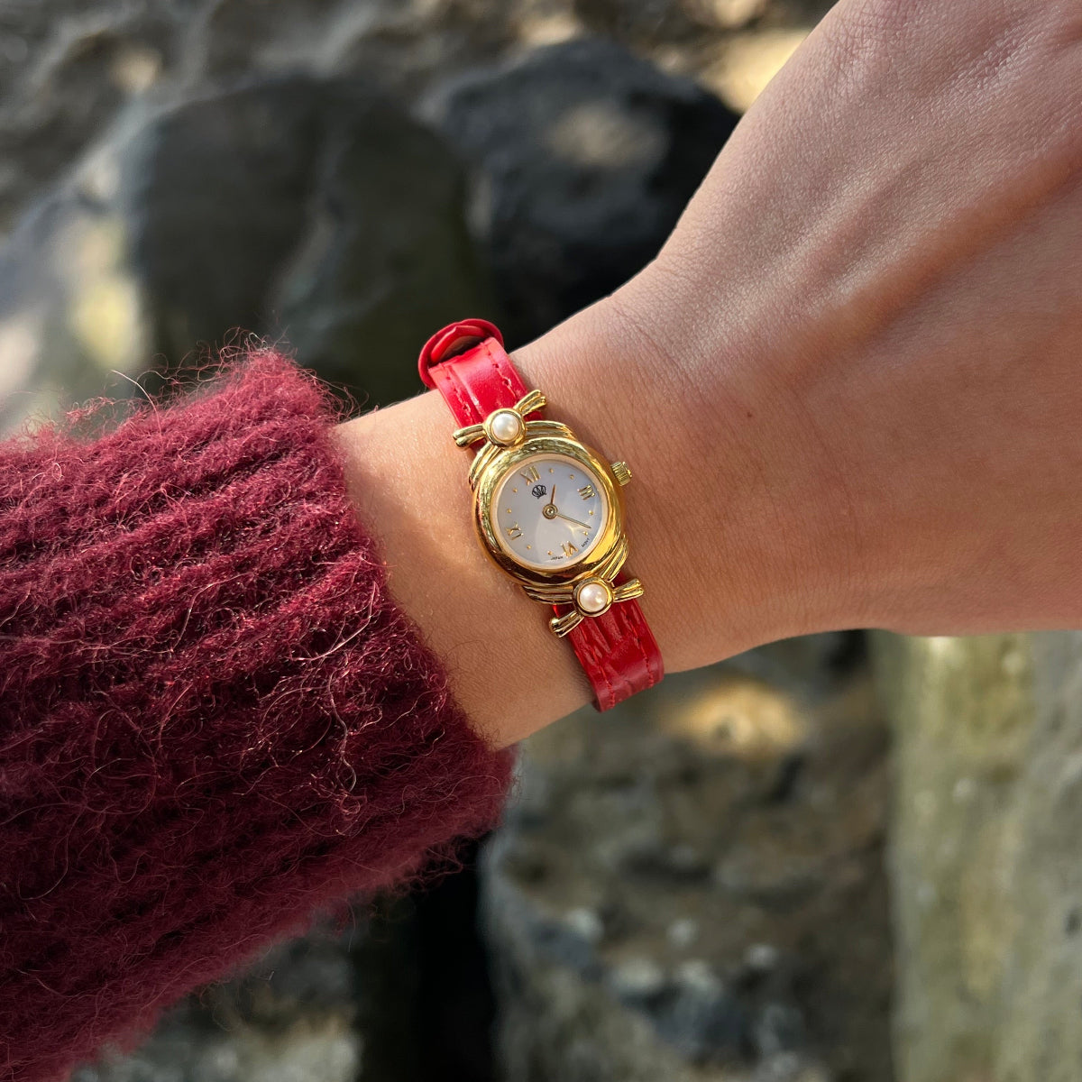 Vintage Mikimoto women’s watch with two Akoya pearls, a mother of pearl dial, sculpted gold ribbon case and original red leather strap worn on the wrist.