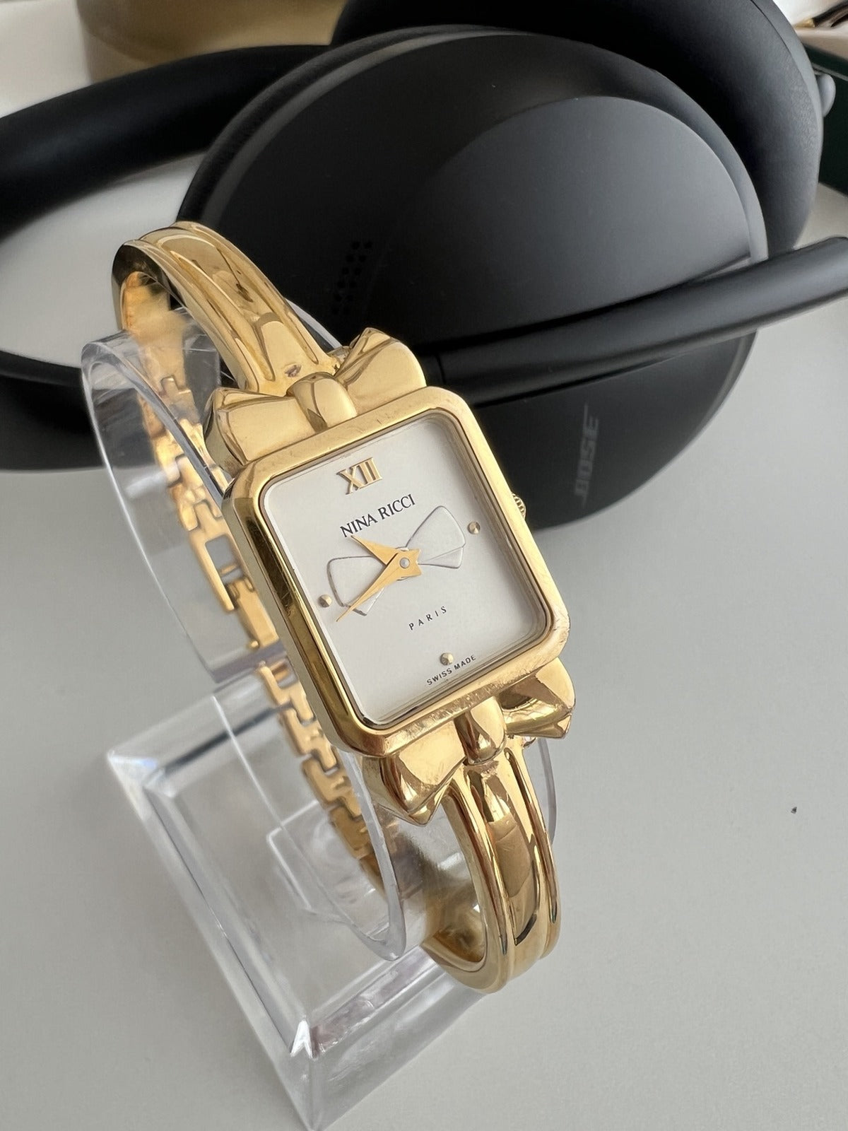 Close view of the Nina Ricci Paris bow dial, rectangular gold plated case and polished fixed position bangle bracelet.