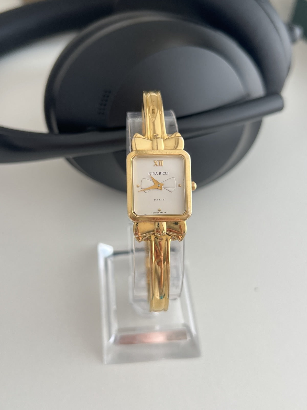 Nina Ricci D950 women’s watch with a rectangular white bow dial and gold plated fixed position bangle, shown front on.