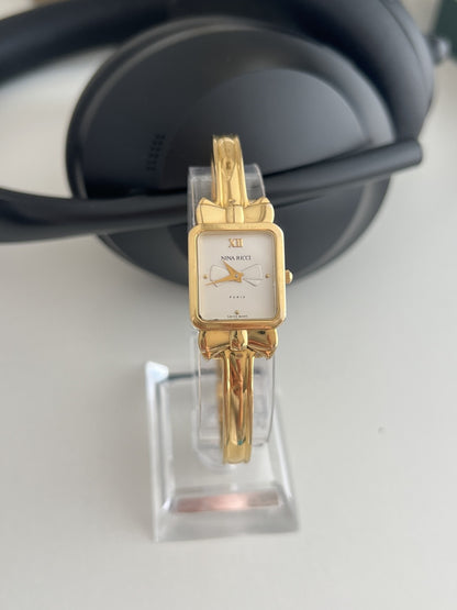 Nina Ricci D950 women’s watch with a rectangular white bow dial and gold plated fixed position bangle, shown front on.
