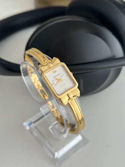 Angled view of the Nina Ricci D950 gold plated women’s watch showing its sculptural bow shoulders and double rail bangle.