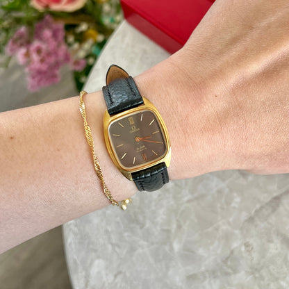Omega De Ville 591.0099 women’s watch with onyx-coloured dial, gold-tone cushion case and black leather strap worn on the wrist