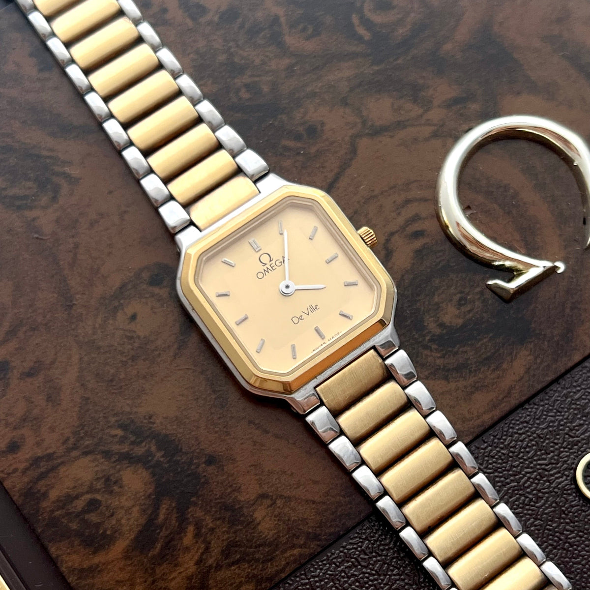 Vintage Omega De Ville America ladies watch with champagne dial and two-tone gold and steel bracelet on a wooden surface.