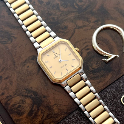 Vintage Omega De Ville America ladies watch with champagne dial and two-tone gold and steel bracelet on a wooden surface.