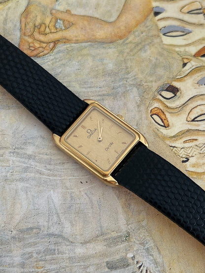 Omega De Ville watch at an angle showing its finely brushed champagne dial, polished gold tone frame and black reptile-pattern strap.