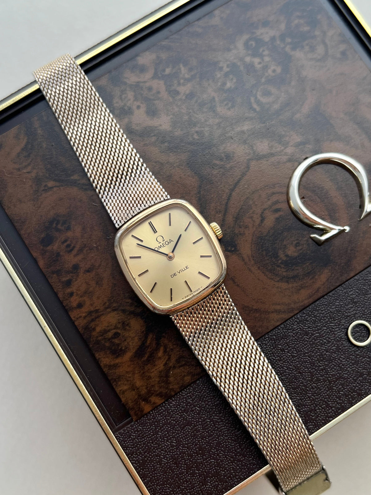 Close view of an Omega De Ville champagne dial with black baton hour markers and a softly squared gold tone case