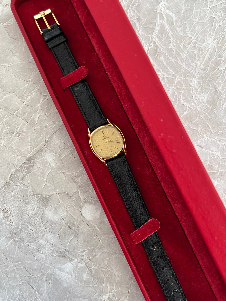Full-length Omega De Ville women's quartz watch with champagne dial and black leather strap photographed in a red watch box