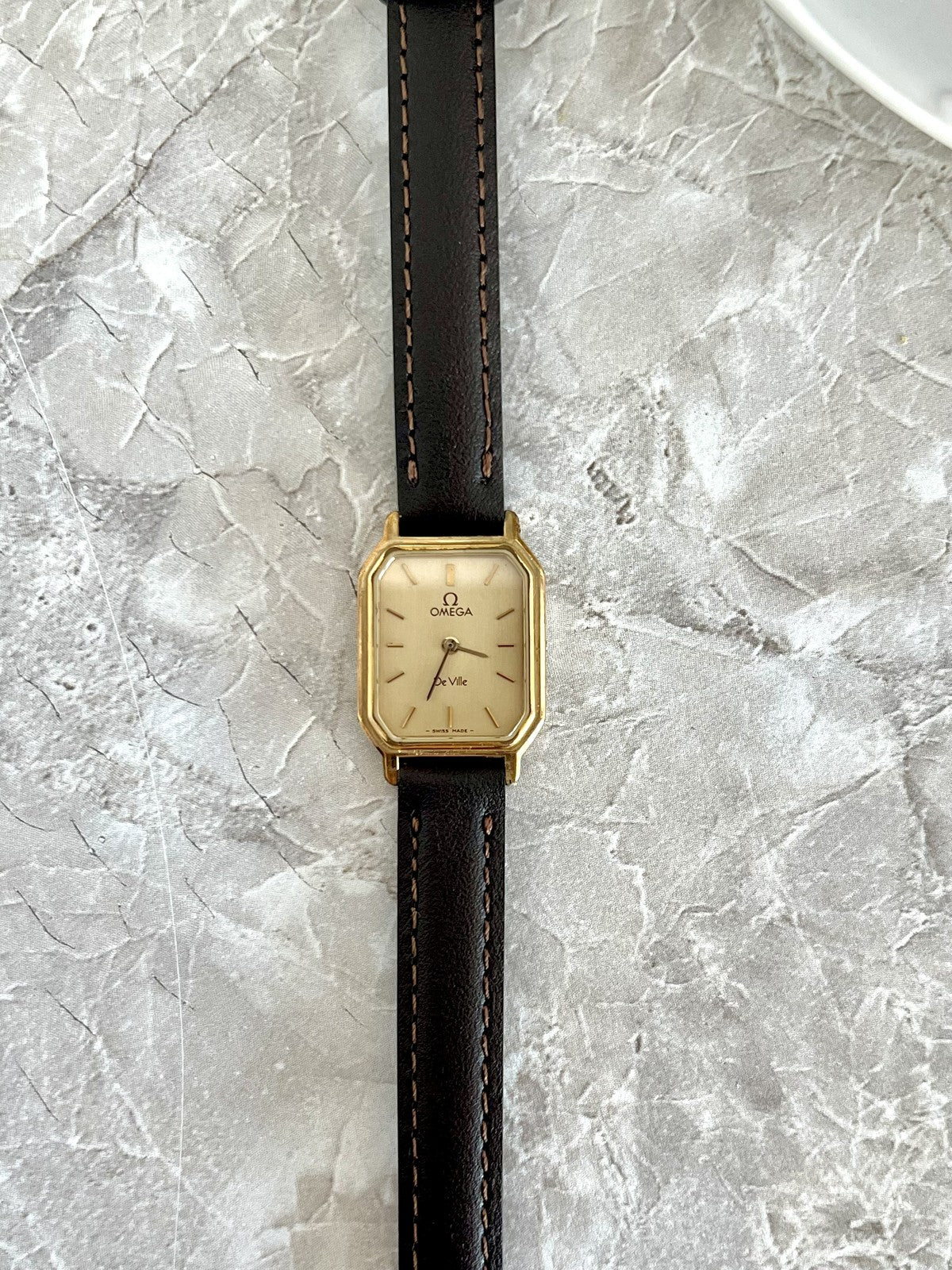 Omega De Ville rectangular women's quartz watch with champagne dial, gold-tone case and dark stitched strap, front view