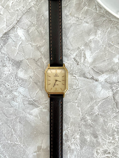 Omega De Ville rectangular women's quartz watch with champagne dial, gold-tone case and dark stitched strap, front view