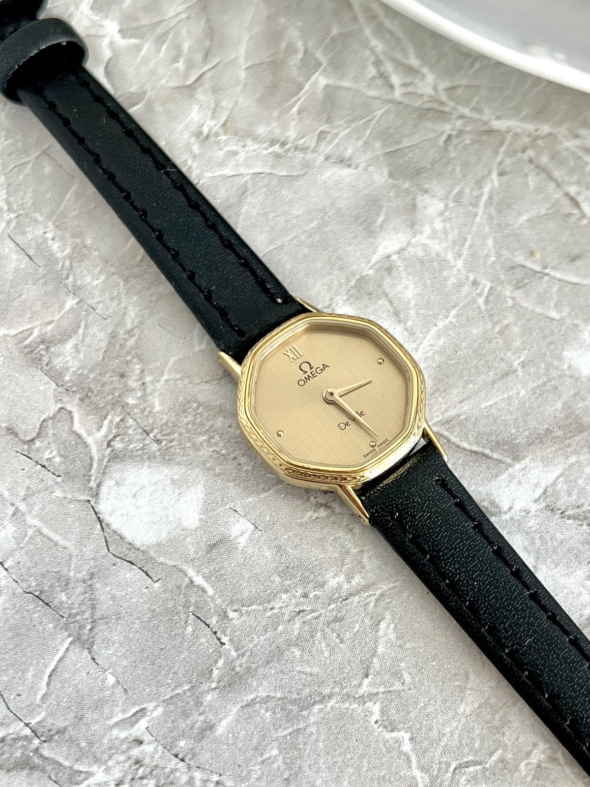 Omega De Ville women's gold-tone cushion watch with champagne textured dial and black strap, front view — ref. 591.0257