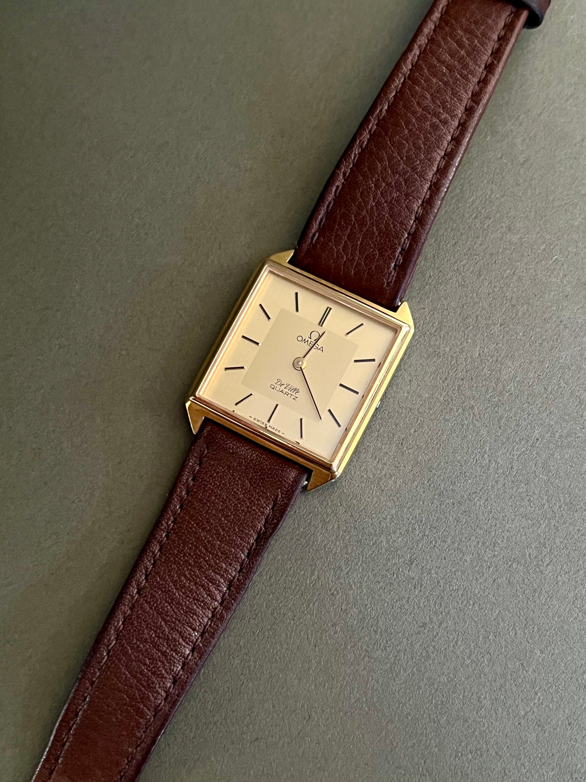Vintage Omega De Ville watch with gold-tone case, champagne dial and brown leather strap.
