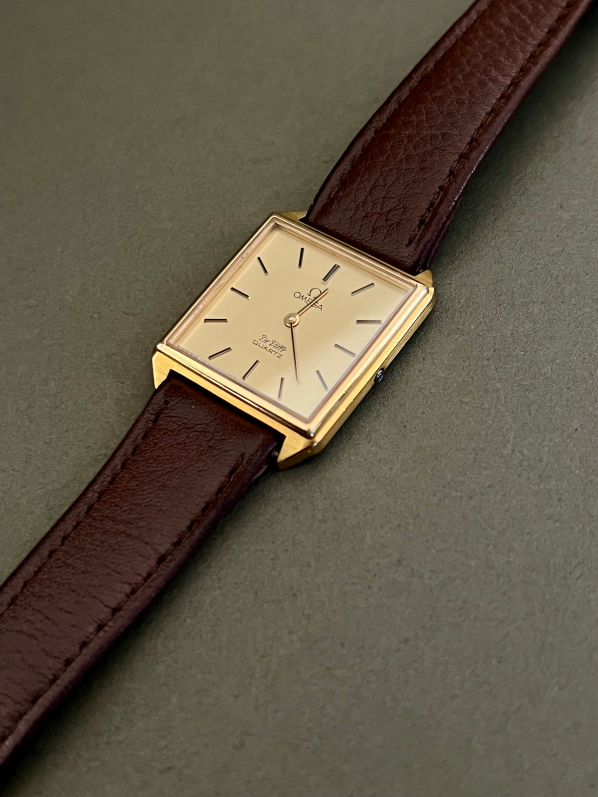 Omega De Ville gold-tone watch with black baton markers and slim hands on a champagne dial.