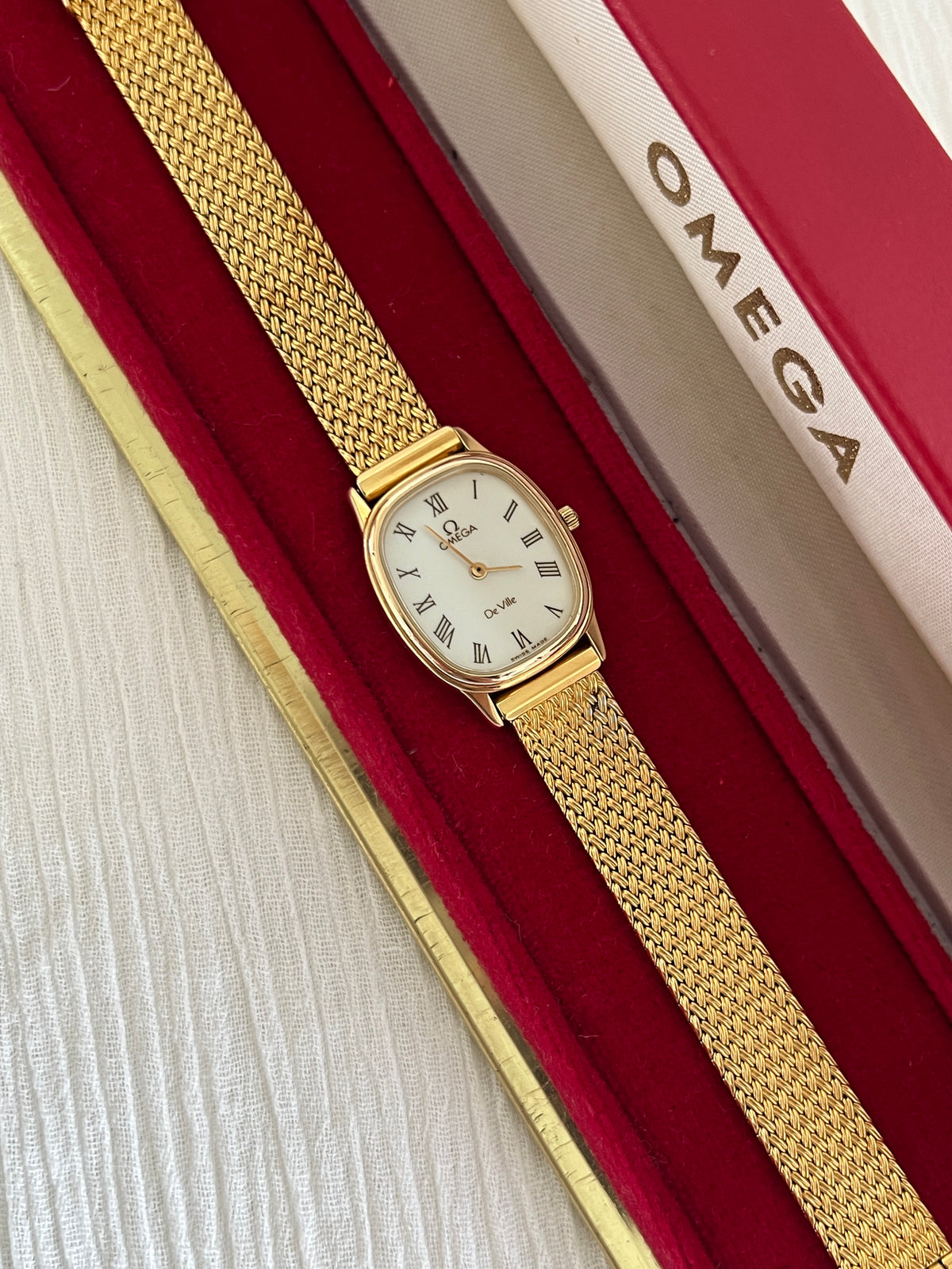 Close-up of the champagne dial with burgundy Roman numerals on the Omega De Ville.