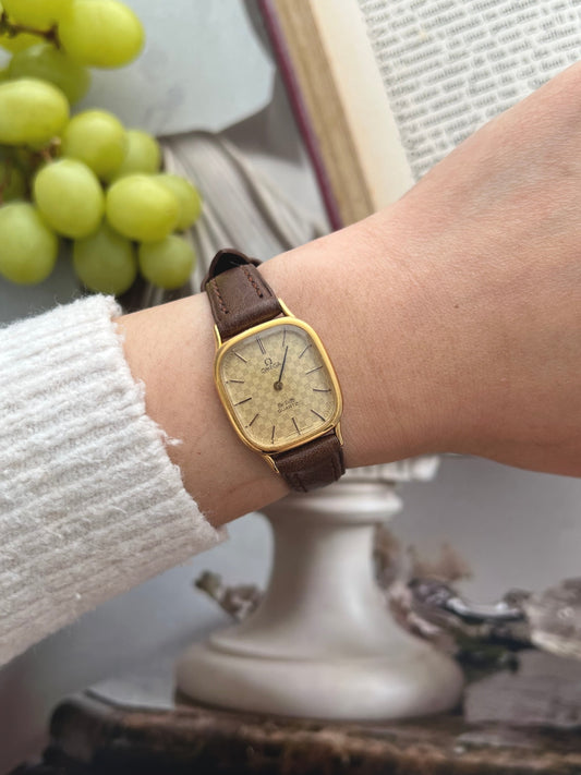 Omega De Ville women's watch with a chequered champagne dial, gold tone cushion case and brown leather strap on the wrist