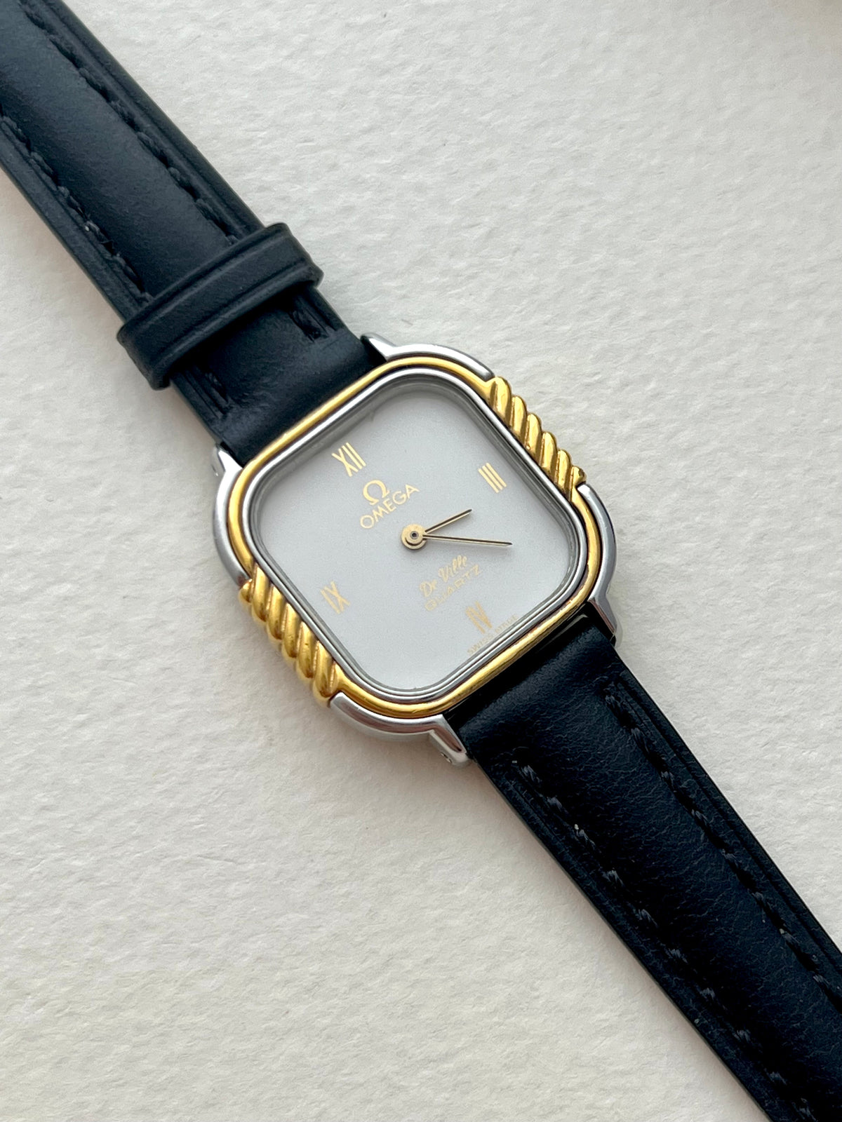 Front view of the Omega De Ville cushion-case ladies watch with white dial and sculpted gold bezel.