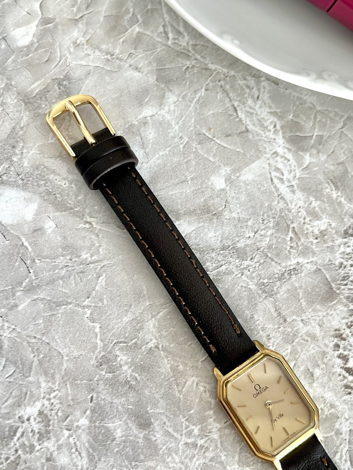Close-up of Omega De Ville watch dark stitched strap and gold-tone pin buckle