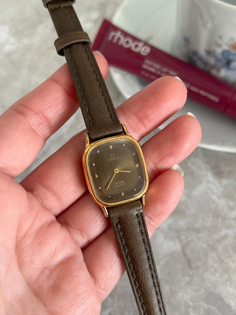 Close-up of Omega De Ville quartz smoked dial with gold dot hour markers and rounded gold-tone case