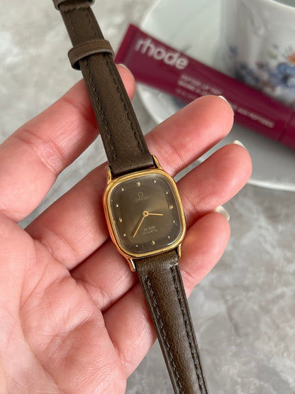 Close-up of Omega De Ville quartz smoked dial with gold dot hour markers and rounded gold-tone case