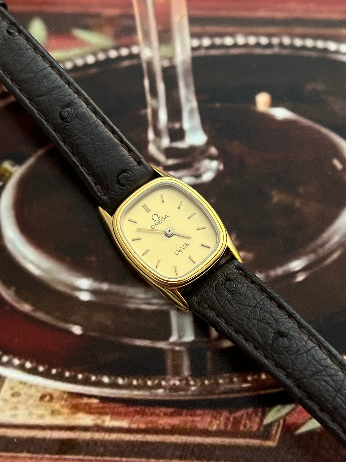Angled view showing the double bezel detail on the small gold-tone Omega De Ville cushion case.