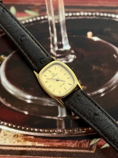 Angled view showing the double bezel detail on the small gold-tone Omega De Ville cushion case.