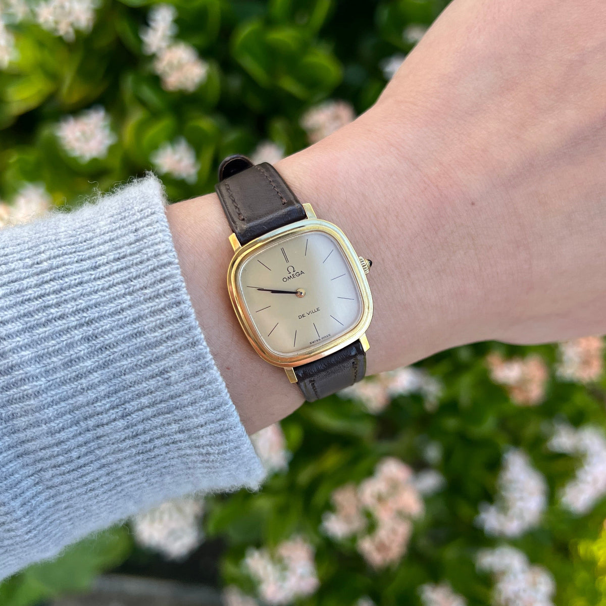 Omega De Ville luxury women’s watch with champagne dial and brown leather strap worn on wrist