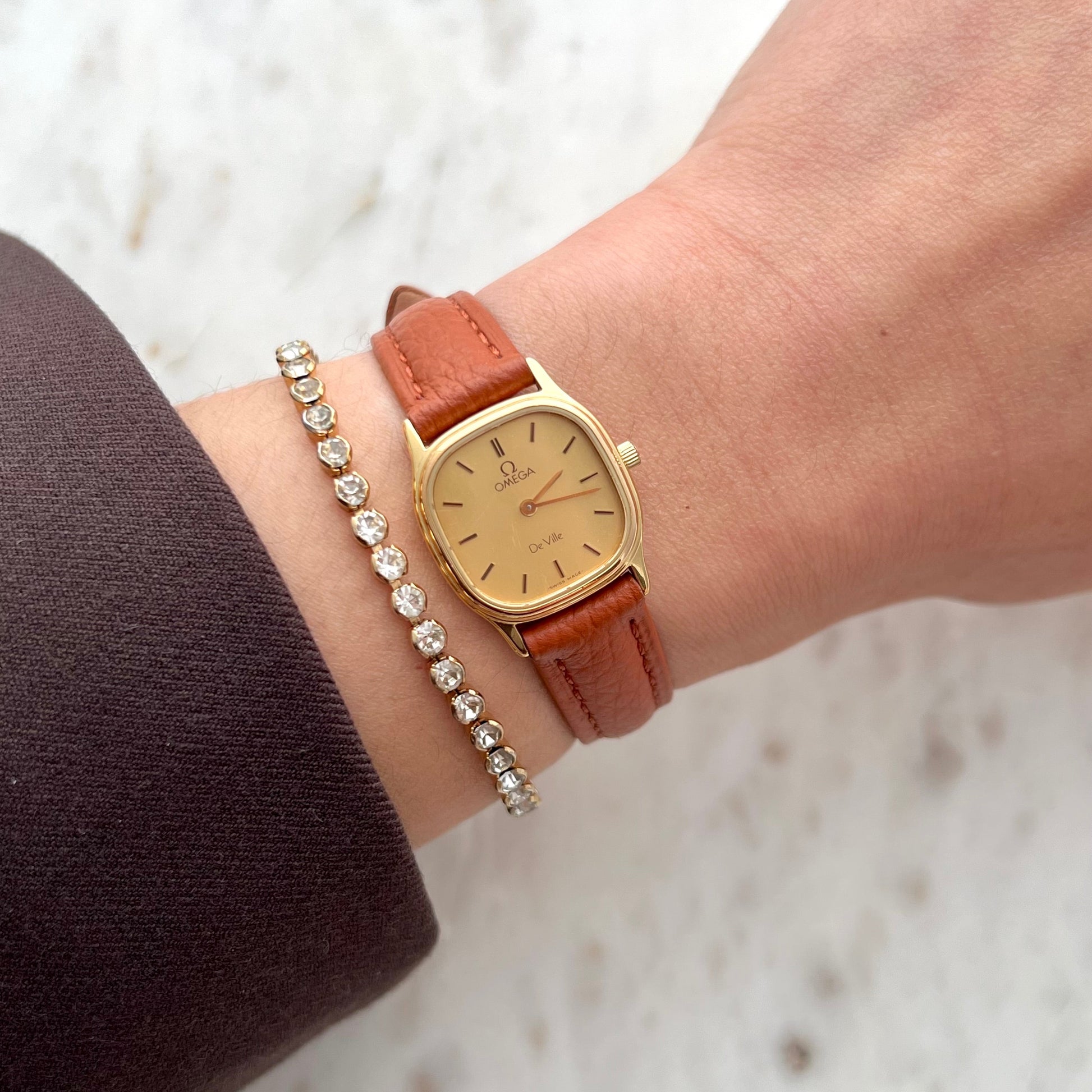 Omega De Ville gold cushion women’s watch with champagne dial and brown leather strap worn on wrist