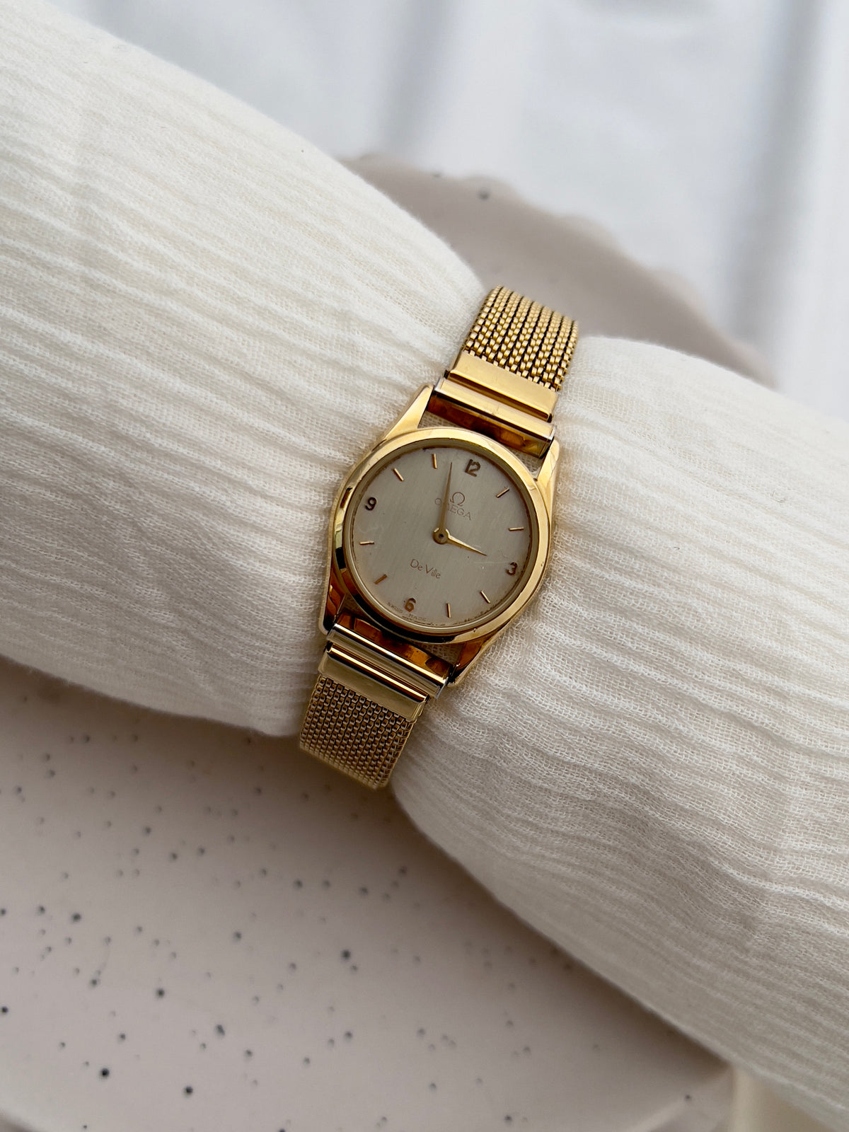 Gold-tone Omega De Ville watch with integrated elastic mesh bracelet.