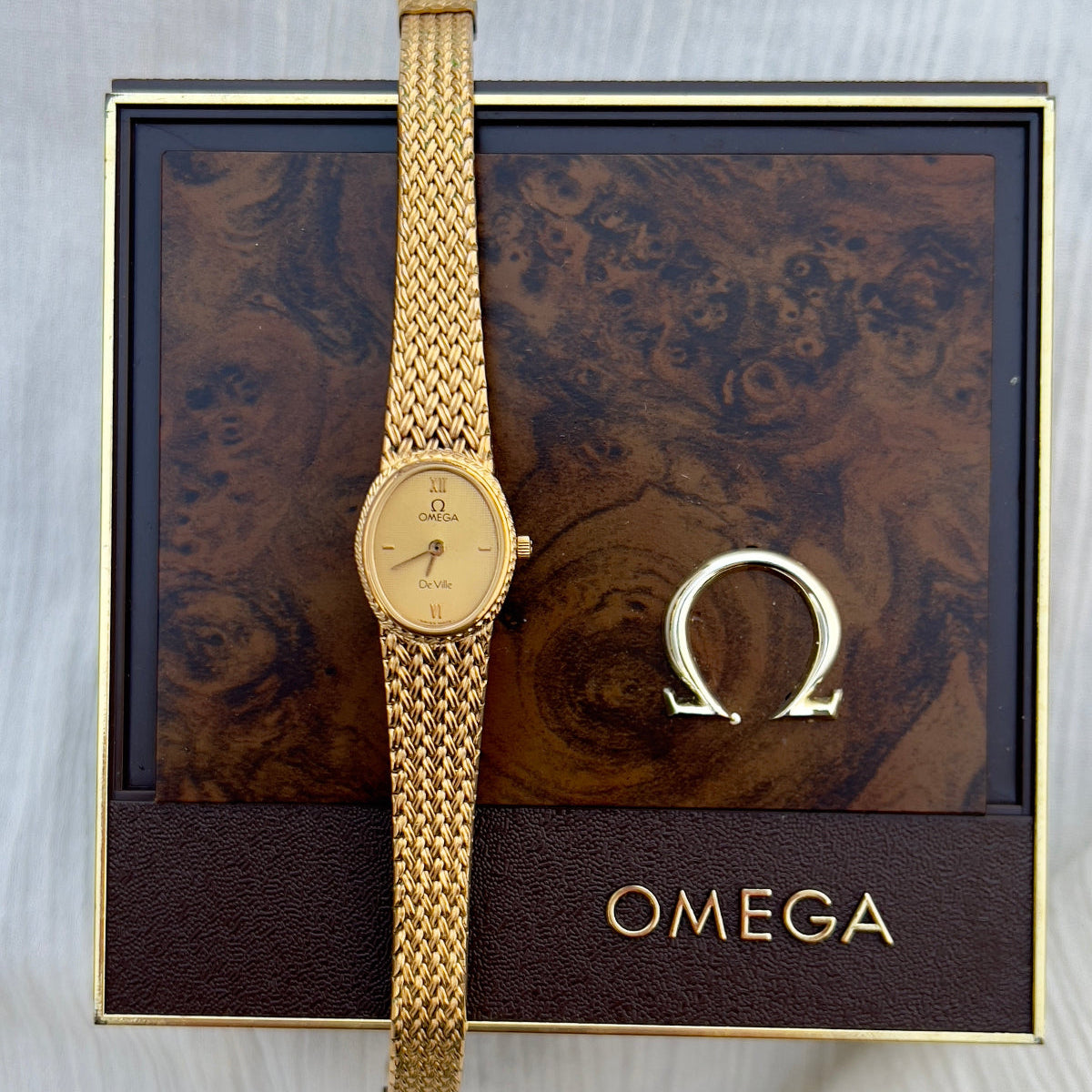 Omega De Ville gold bracelet watch with champagne guilloché dial and woven wheat-link bracelet.