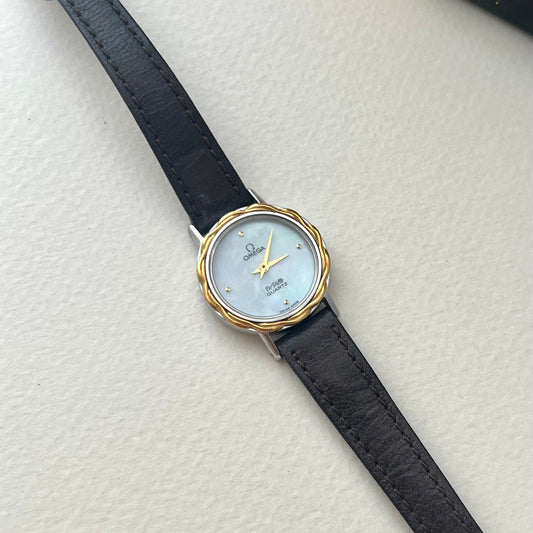 Omega De Ville ladies watch with luminous mother-of-pearl dial, sculpted gold laurel bezel and woven gold-tone bracelet.