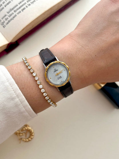 Front view of the Omega De Ville watch with mother-of-pearl dial, gold laurel bezel and woven bracelet.