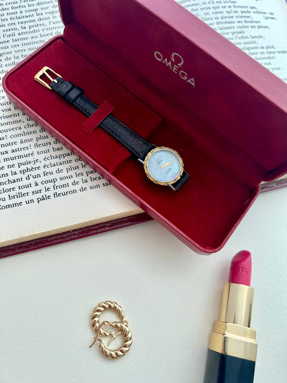 Omega De Ville mother-of-pearl watch with gold-tone woven bracelet shown on the wrist.