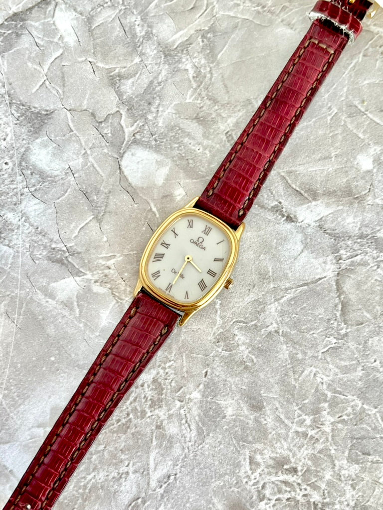 Angled view of gold-tone Omega De Ville oval dress watch on a red crocodile-pattern strap