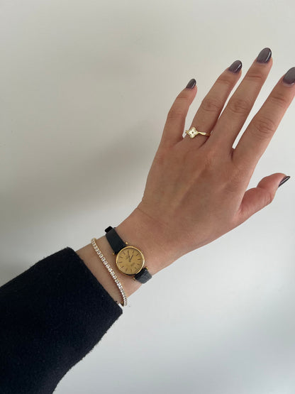 Omega De Ville gold-tone watch with black leather strap shown on a wrist.