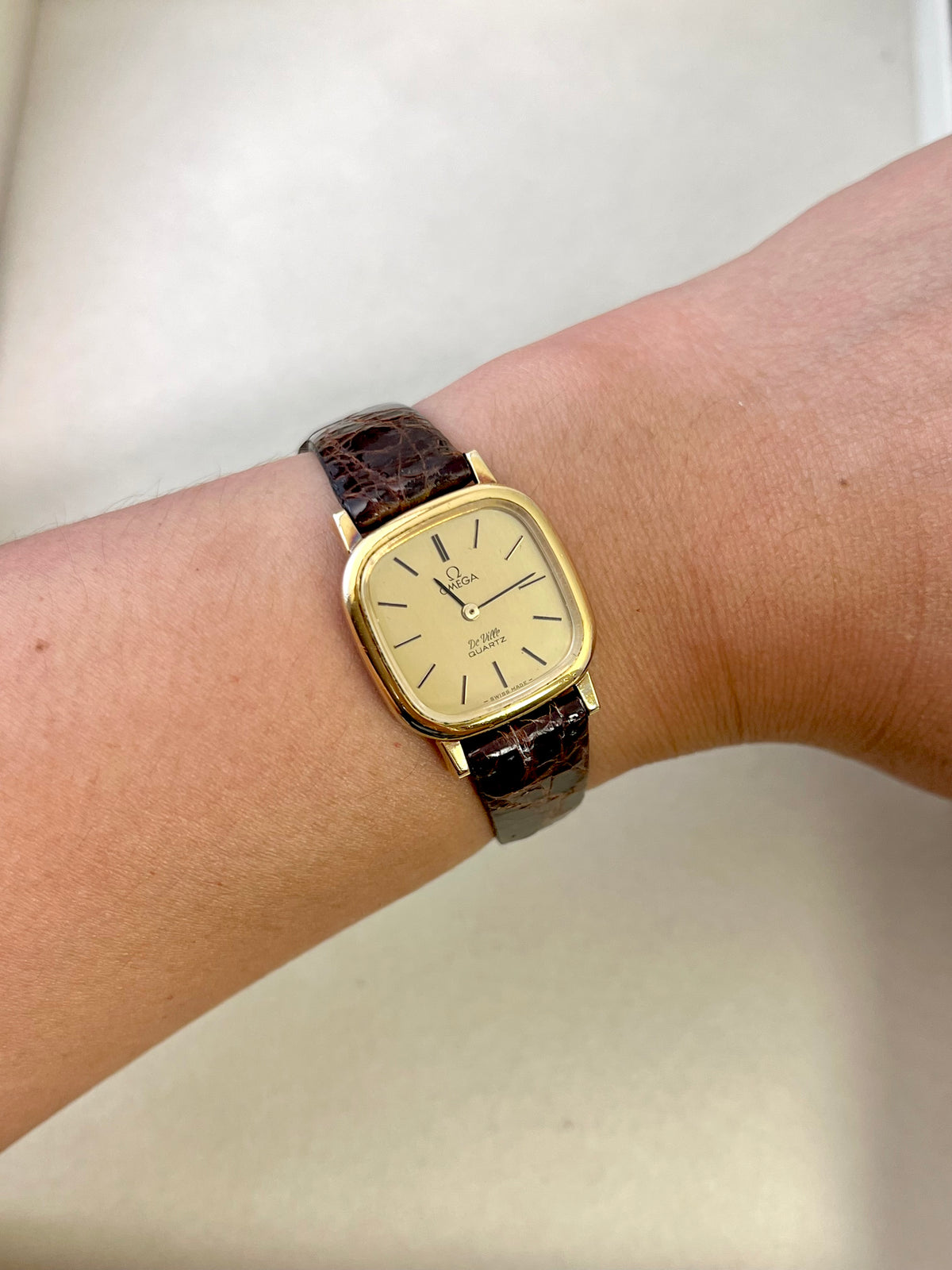 Front view of the Omega De Ville gold square watch with champagne dial and black leather strap.