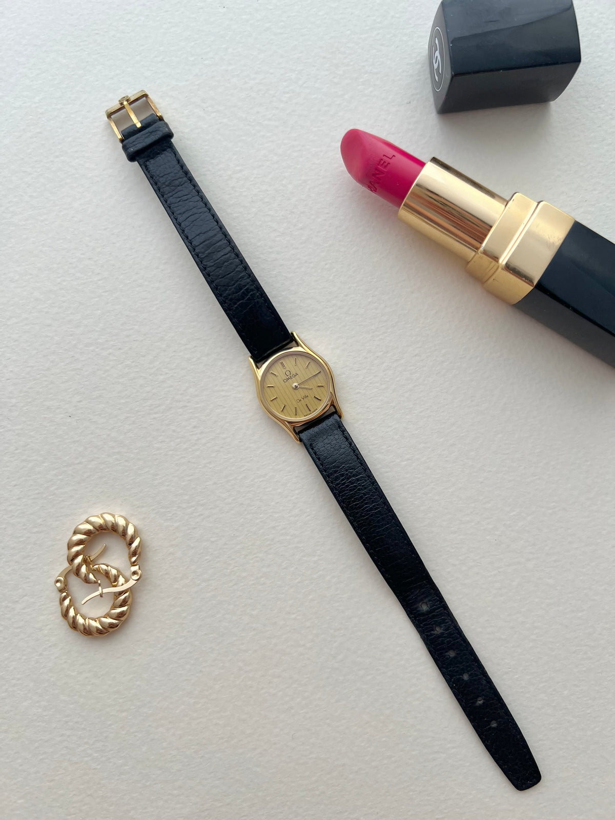 Vintage Omega De Ville watch with round gold-tone case and textured dial.