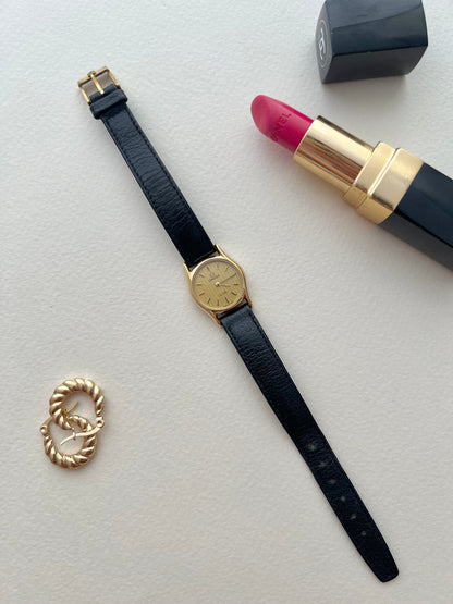 Vintage Omega De Ville watch with round gold-tone case and textured dial.