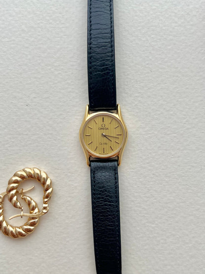 Omega gold watch with black-accented markers and baton hands.