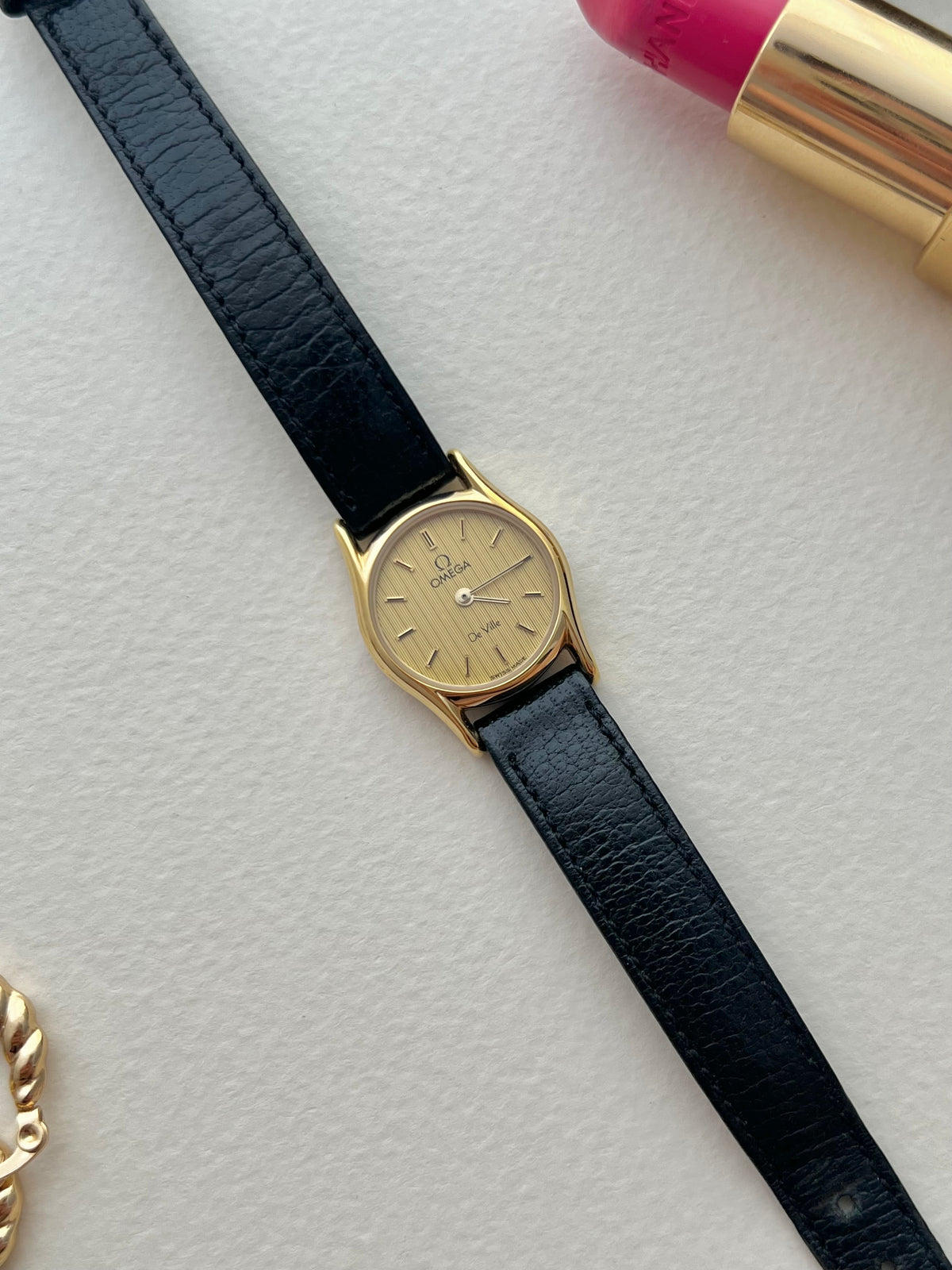 Omega De Ville gold-tone watch with soft lugs and patterned dial.