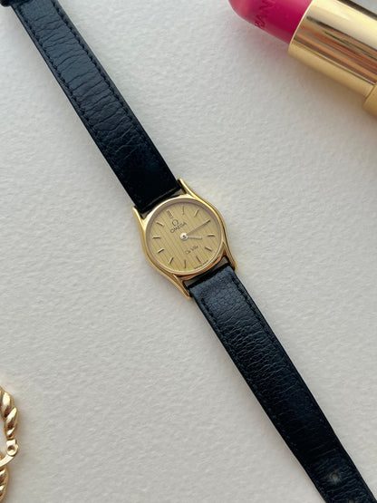 Omega De Ville gold-tone watch with soft lugs and patterned dial.