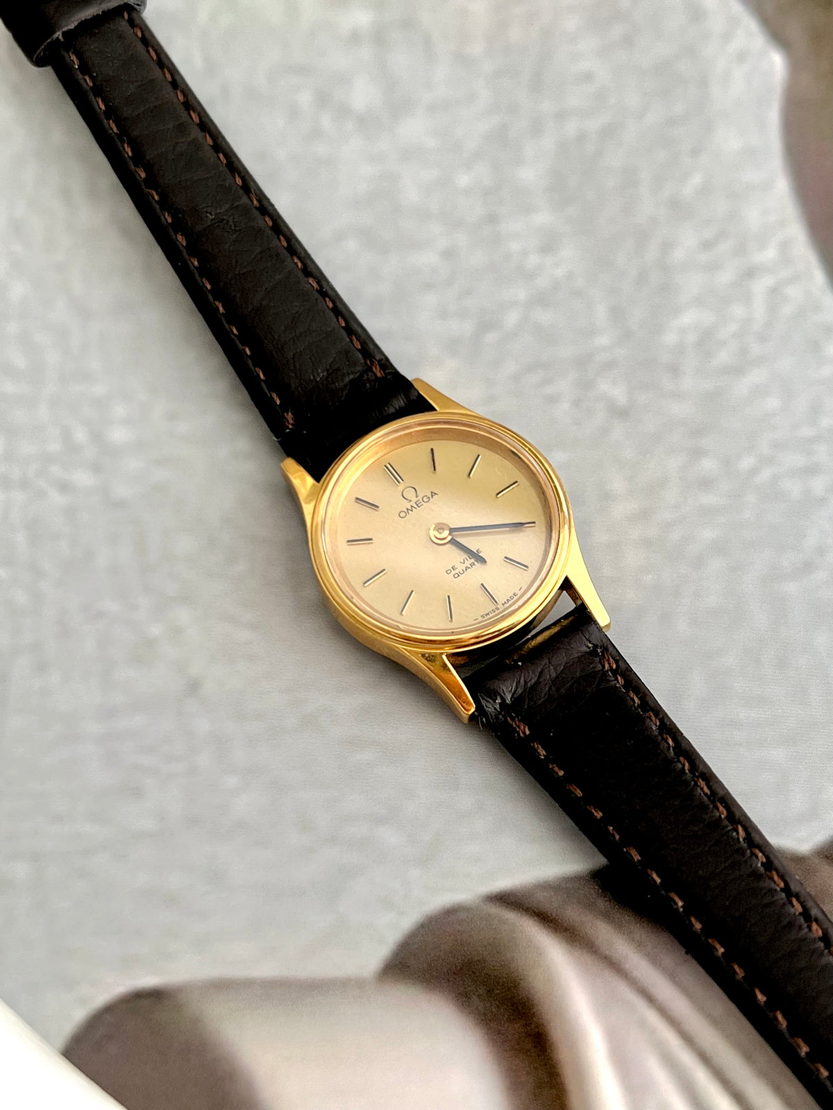 Omega De Ville gold-tone watch with brown leather strap shown on a wrist.