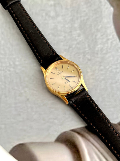 Omega De Ville gold-tone watch with brown leather strap shown on a wrist.