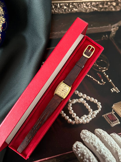 Full view of the Omega De Ville gold tone tonneau watch and brown lizard strap inside the open red Omega presentation box.